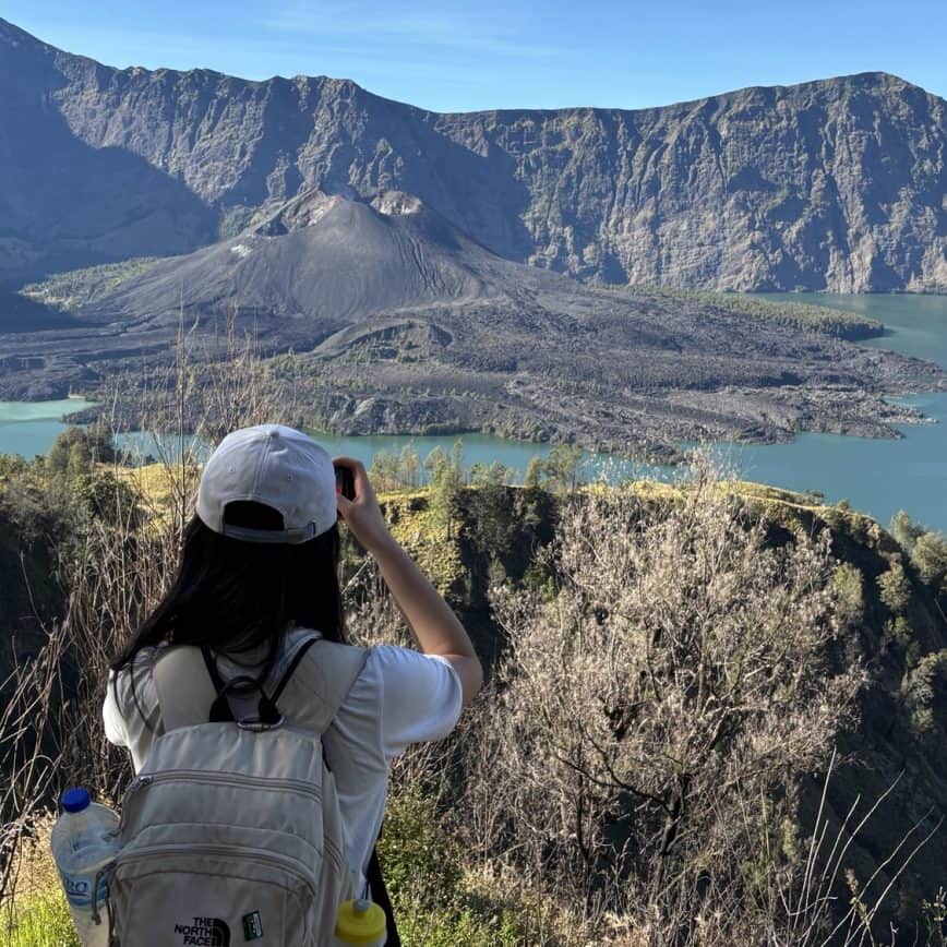 The serene view of Lake Segara Anak on Mt Rinjani at sunset, with a vibrant sky reflected on the calm water and the volcano's crater rim silhouetted in the background.