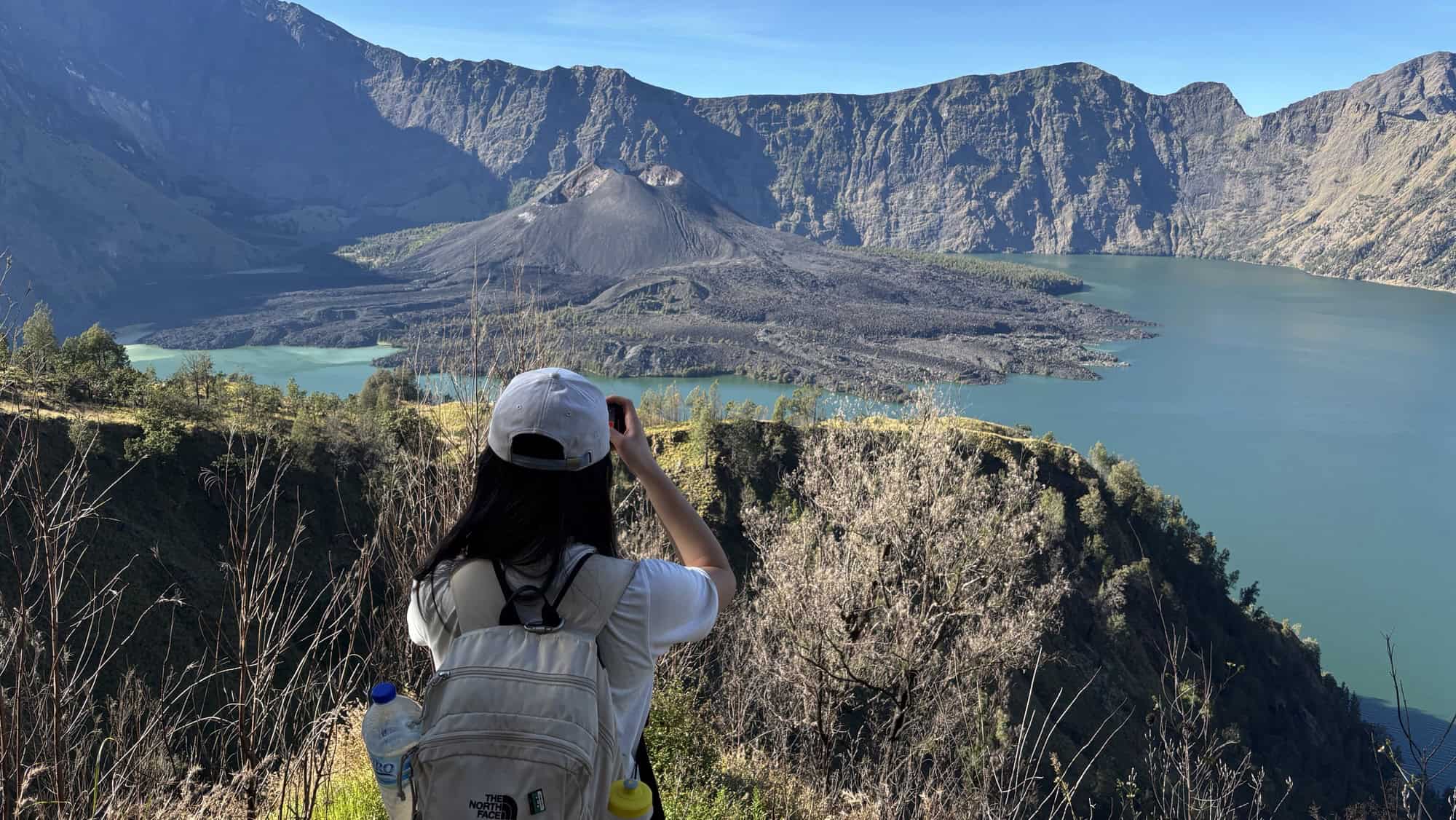 The serene view of Lake Segara Anak on Mt Rinjani at sunset, with a vibrant sky reflected on the calm water and the volcano's crater rim silhouetted in the background.