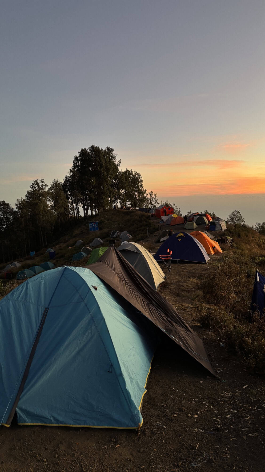 Tents are pitched on a campsite on Mt Rinjani's slopes as the sun sets, casting a warm glow over the landscape.