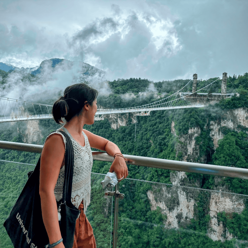 Woman looking at Zhangjiajie Glass Bridge in misty canyon