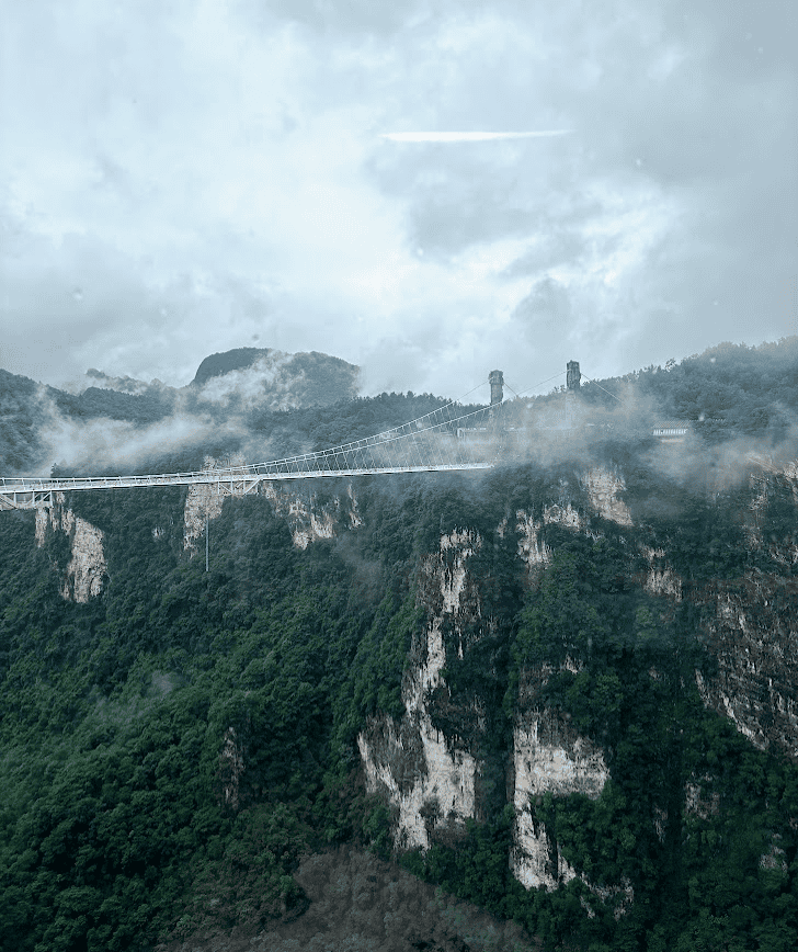 Wide view of the Zhangjiajie Glass Bridge suspended over the misty canyon