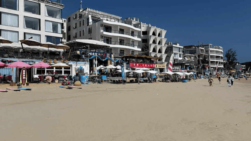 Beachfront hotels and surf schools lined along the sandy shore of Houhai Bay in Sanya, Hainan.