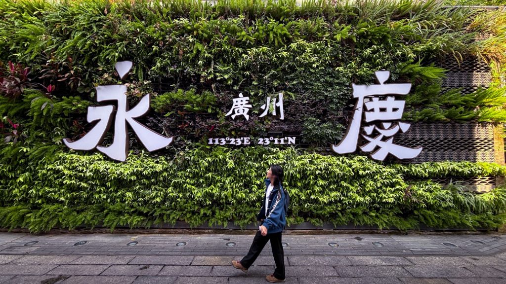 A traveler walking past the famous green wall at Enqing Fang during a Guangzhou day trip.