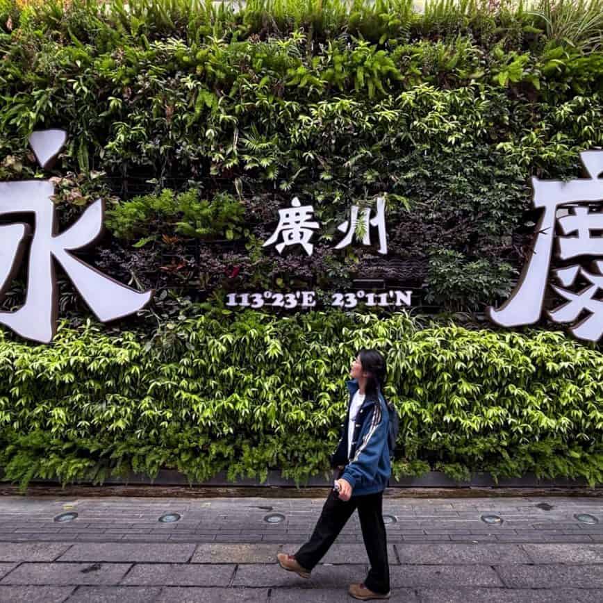 A traveler walking past the famous green wall at Enqing Fang during a Guangzhou day trip.