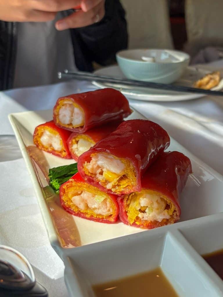 Bright red crispy shrimp rice rolls served on a white rectangular plate with dipping sauces.