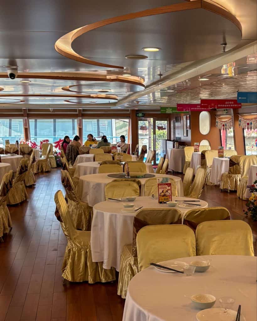 The interior of a river cruise boat featuring round dining tables with gold chair covers.