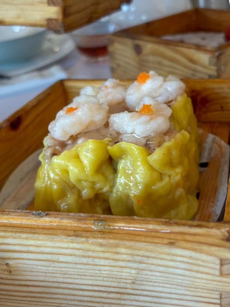 Close up of yellow shrimp shumai dim sum in a wooden steamer box.