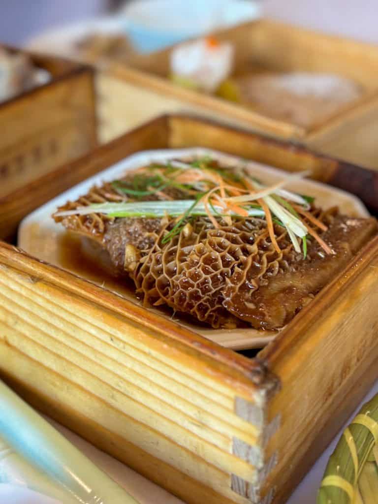 Slices of steamed beef tripe with ginger and scallions in a wooden box.
