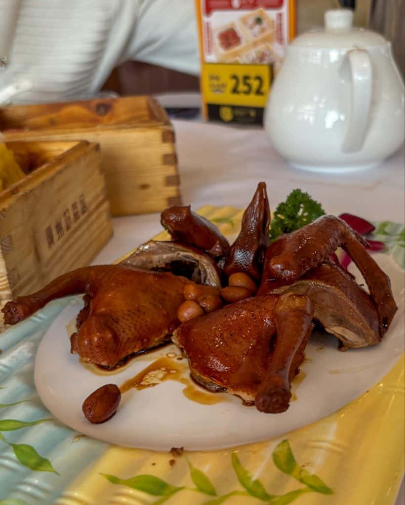 Pieces of dark brown roasted pigeon served on a white plate with a green garnish.