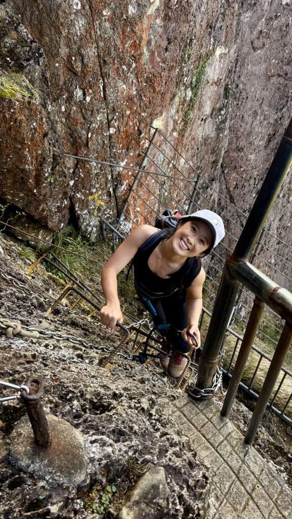 A vertical rock face at Qixian Ridge with metal chains and hikers climbing toward the summit.