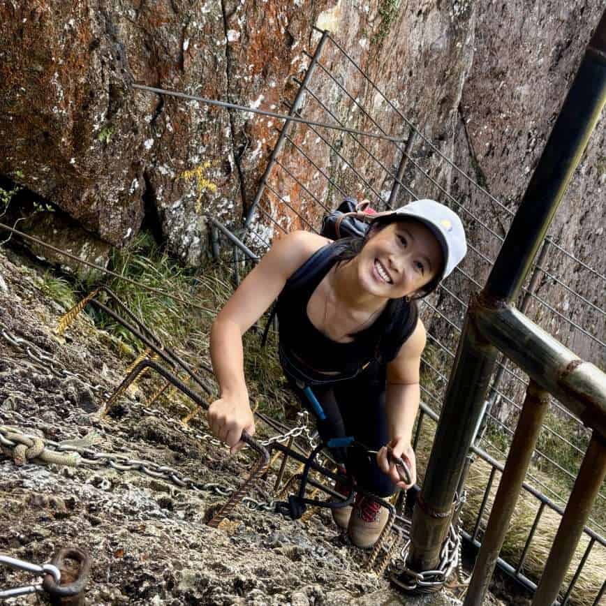 A vertical rock face at Qixian Ridge with metal chains and hikers climbing toward the summit.