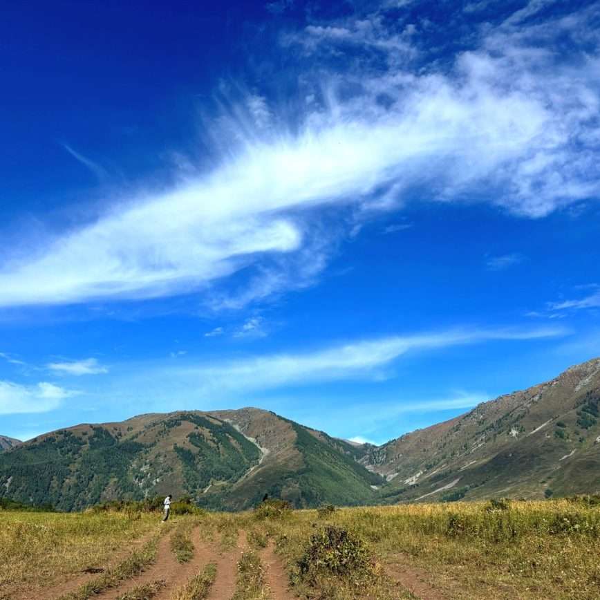 Wide valley view from the horse riding route to Beauty Peak in Hemu Village, green mountains under a bright blue sky with wispy clouds