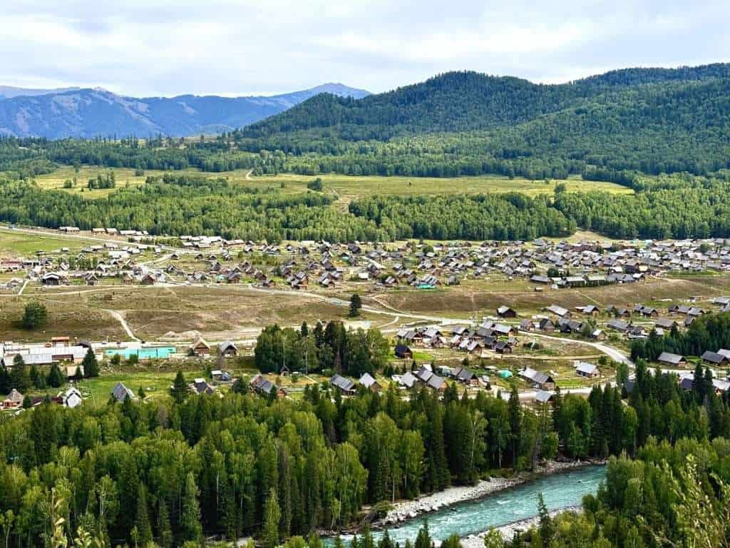 Aerial view of Hemu Village from Hadeng Viewing Platform, wooden cabins scattered across a green valley beside a turquoise river