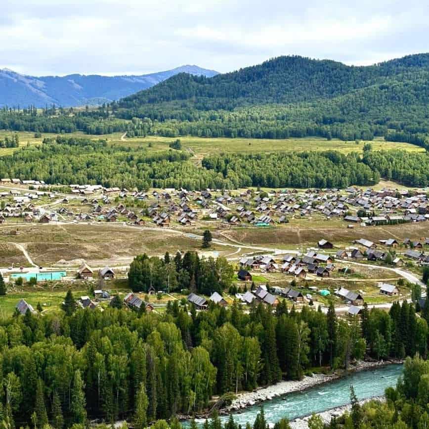 Aerial view of Hemu Village from Hadeng Viewing Platform, wooden cabins scattered across a green valley beside a turquoise river