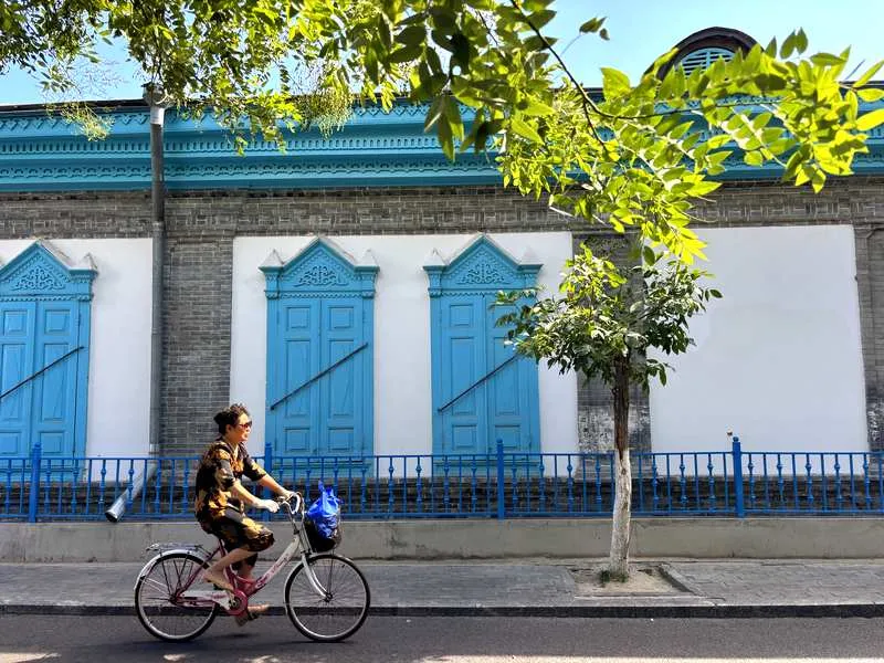 A cyclist rides past the blue-shuttered courtyard walls of Kazanchi Yining Xinjiang