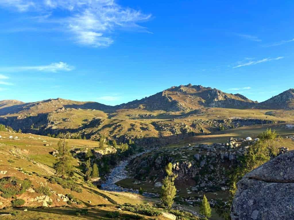 Rolling grassland scenery along the Ahe Highway with distant peaks and low cloud
