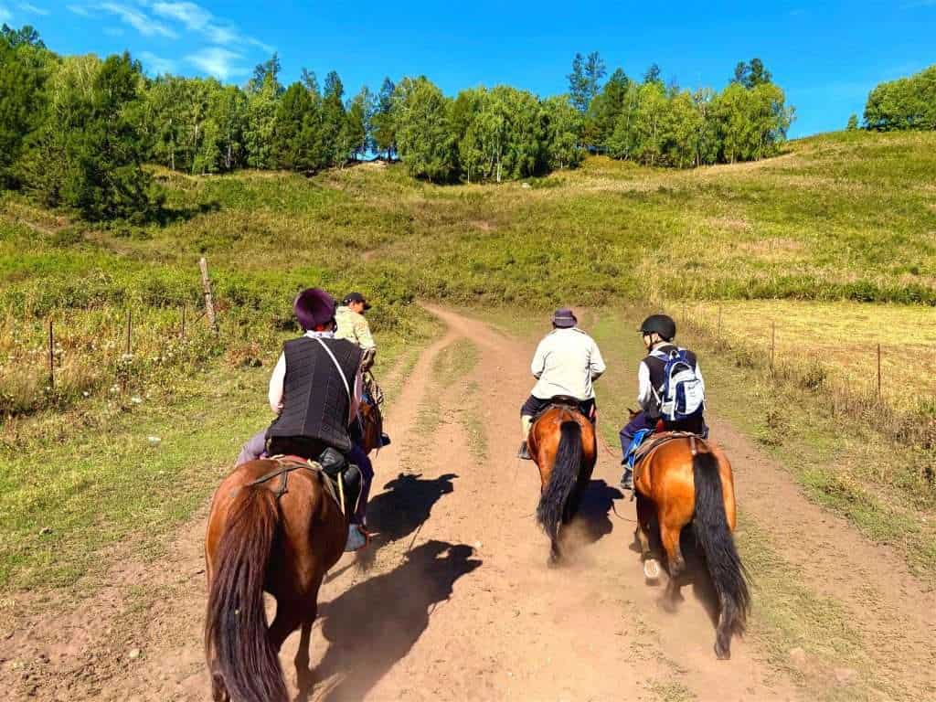 Two horse riders and their guide on the trail to Beauty Peak in Hemu Village, green hills and forest in the background